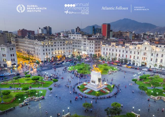 A vibrant evening view of Plaza San Martín in Lima, Peru, showcasing the illuminated colonial buildings surrounding the square. The plaza is bustling with people enjoying the scenic setting, lush green gardens, and the iconic equestrian statue of José de San Martín at its center. The backdrop includes modern city buildings and the Andes mountains under a dusky blue sky